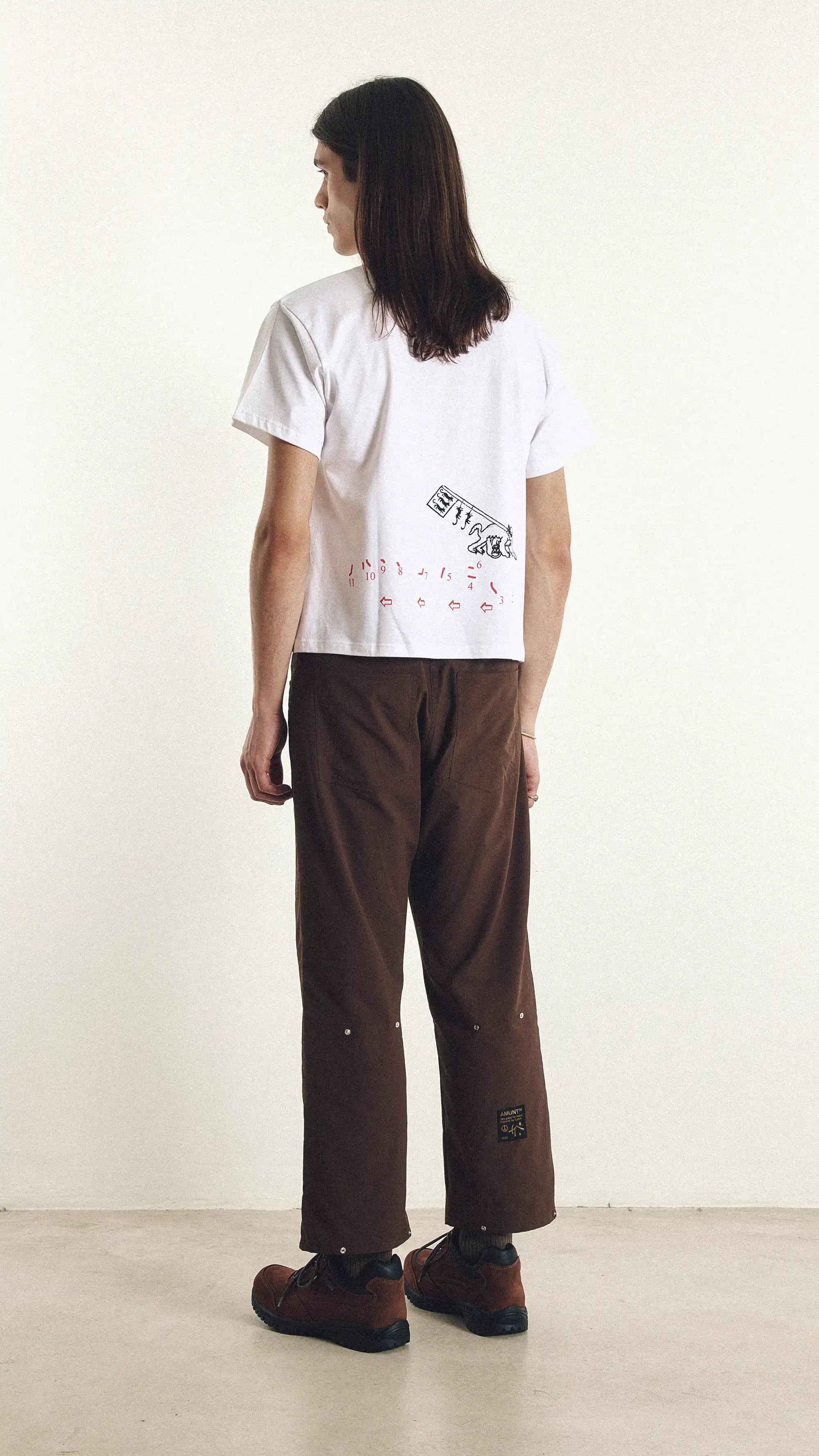 Person wearing a white t-shirt with a logo and brown pants on a white background