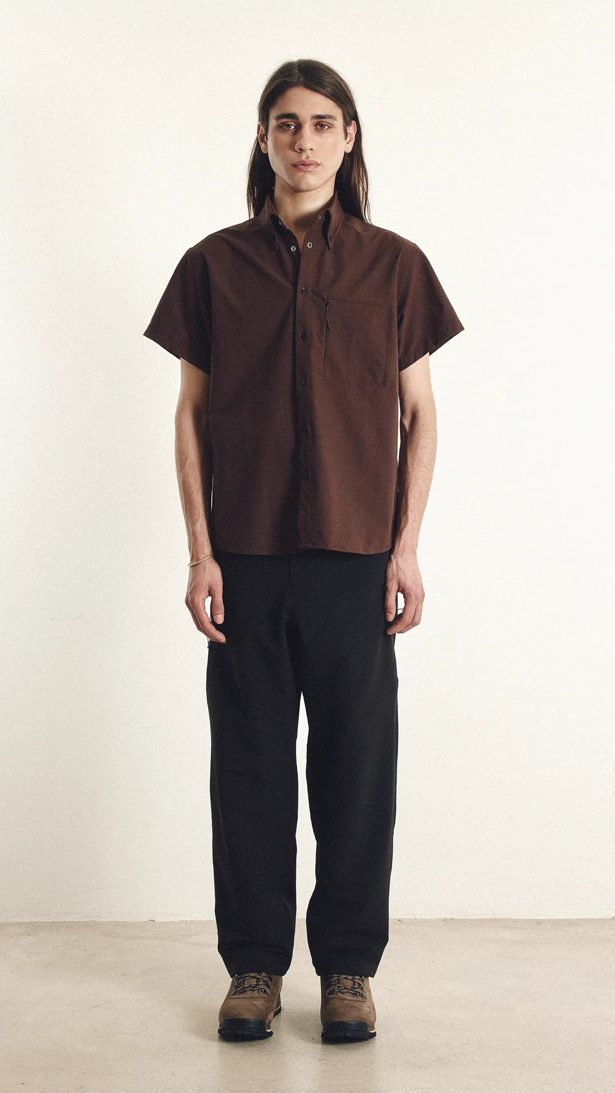 Person wearing a brown shirt and black pants on a white background