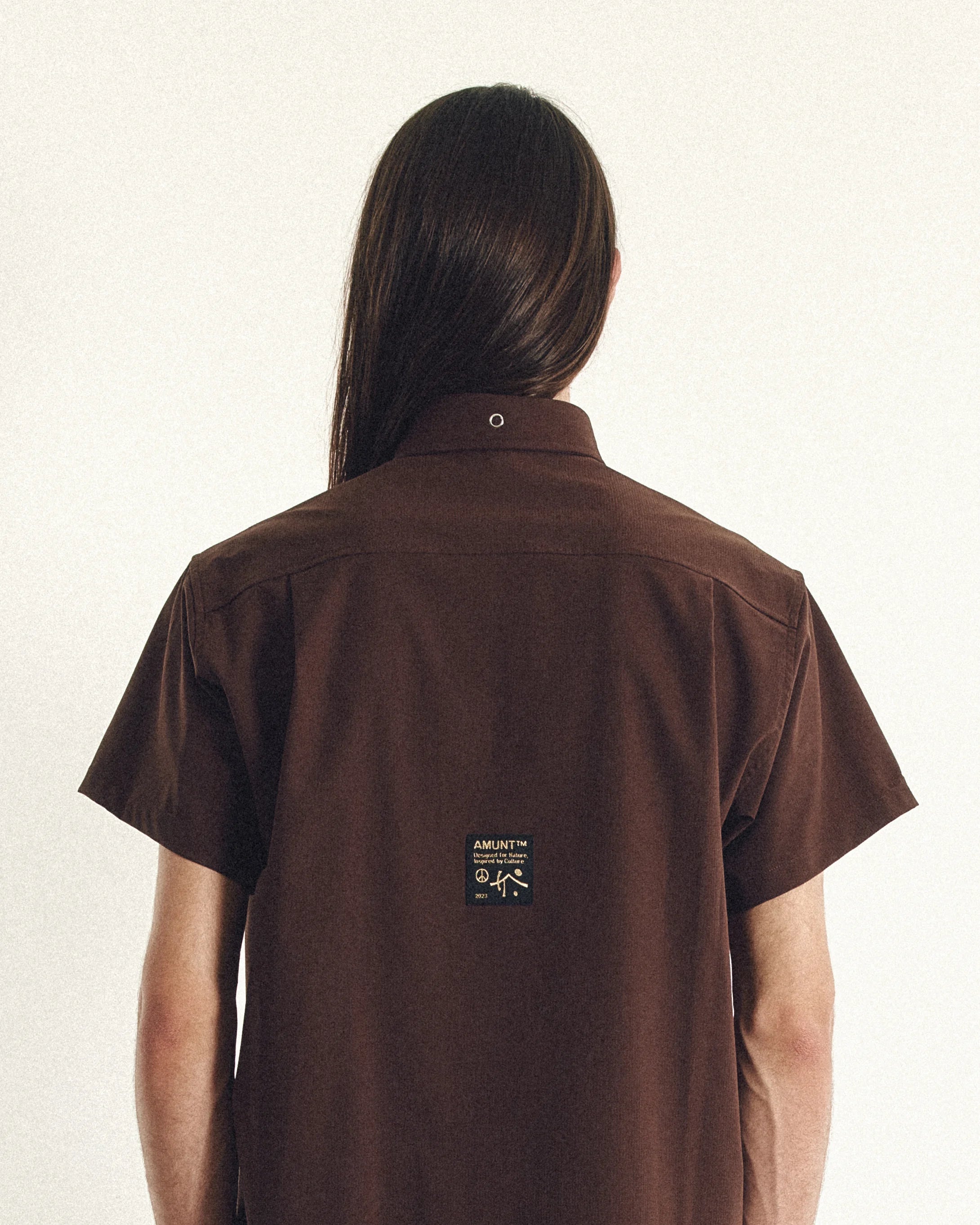 Person wearing a brown shirt with a logo on the back against a white background