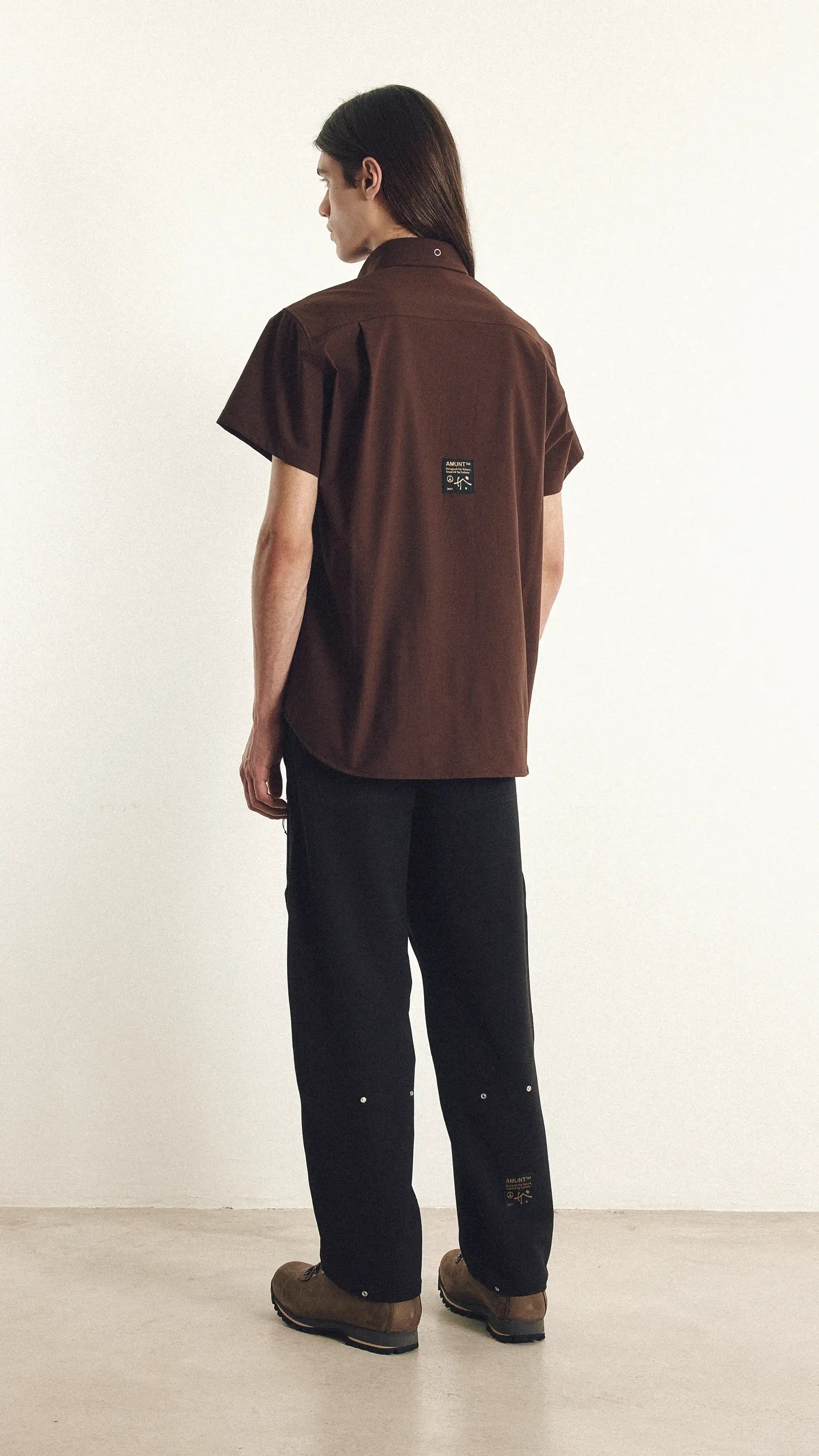 Person wearing a brown shirt and black pants against a white background