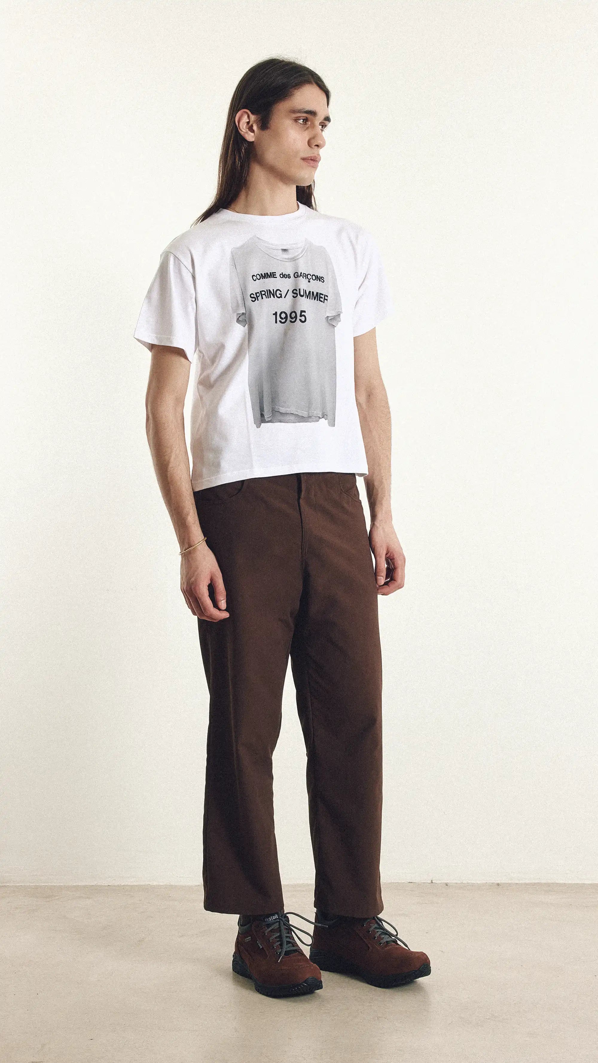 Person wearing a white t-shirt with text and brown pants on a plain background