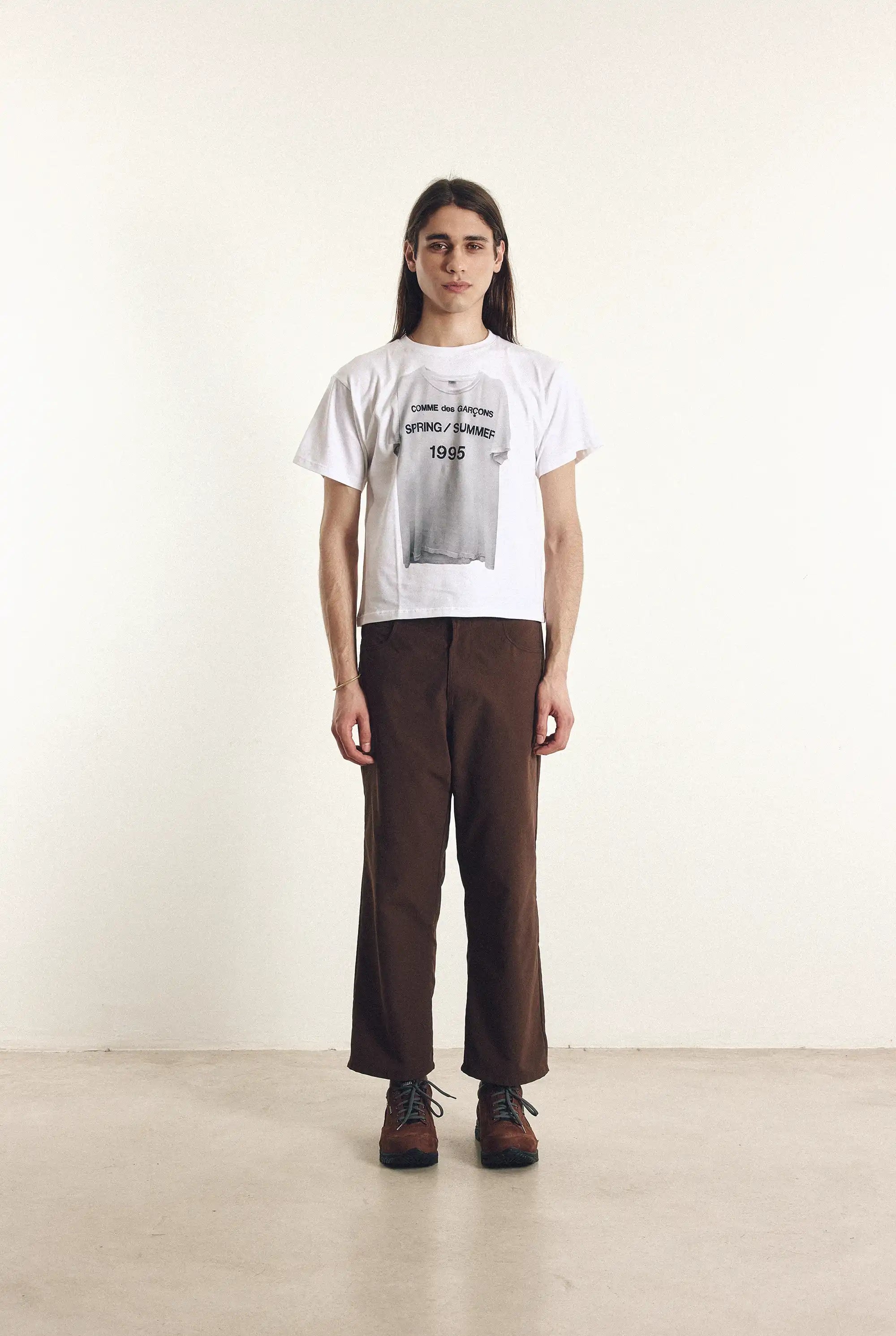 Person wearing a white t-shirt with text and brown pants on a plain background