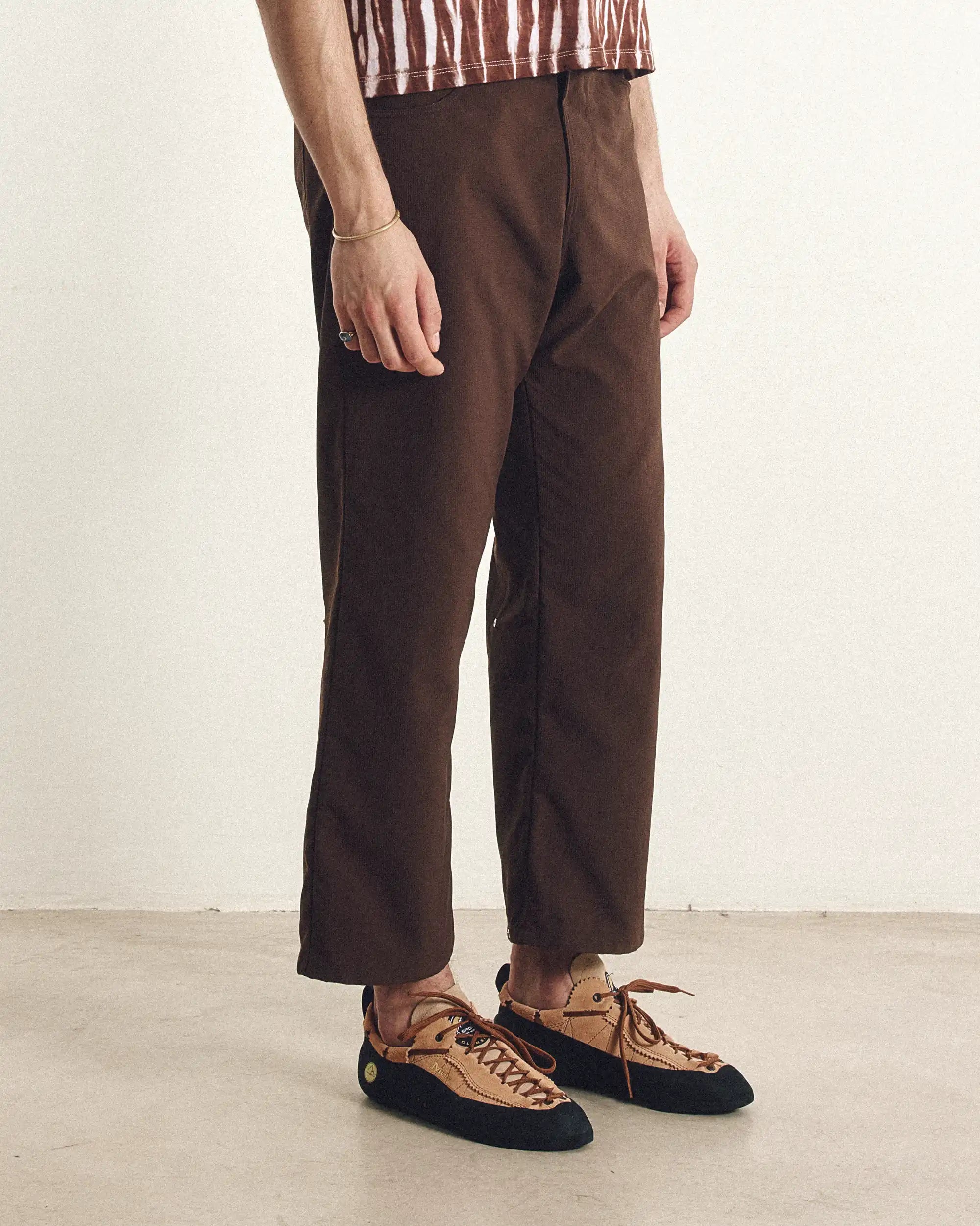 Person wearing brown pants and a striped shirt, standing against a plain background