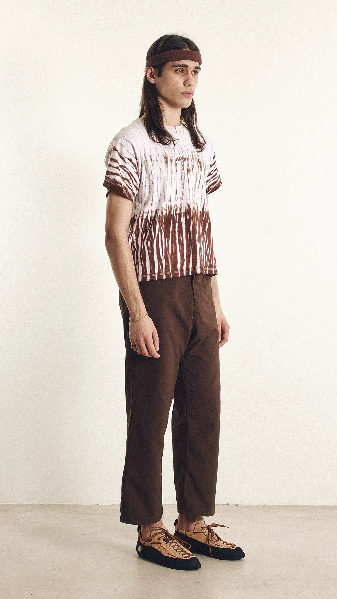 Person wearing a tie-dye shirt and brown pants on a white background