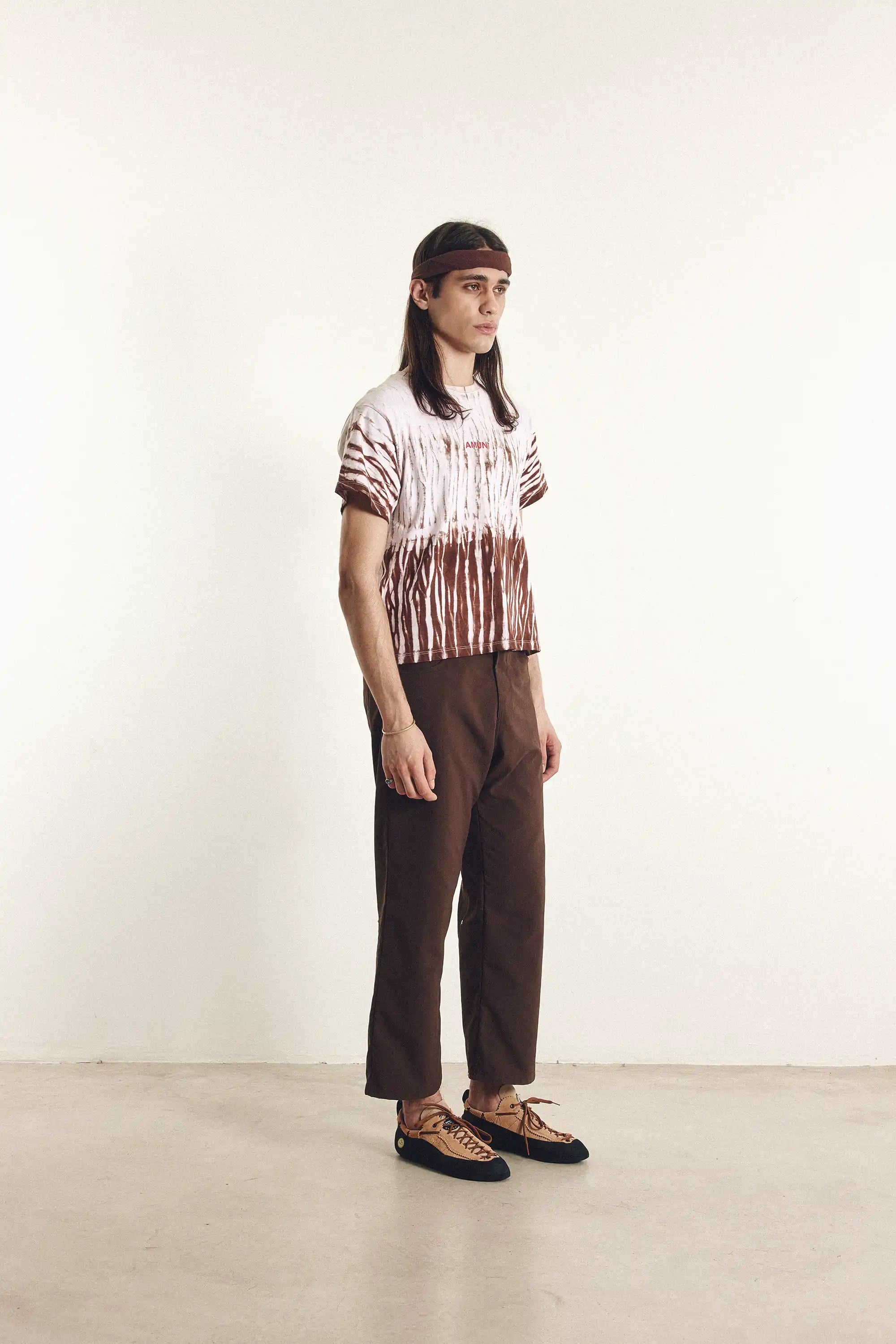 Person wearing a tie-dye shirt and brown pants standing against a white background