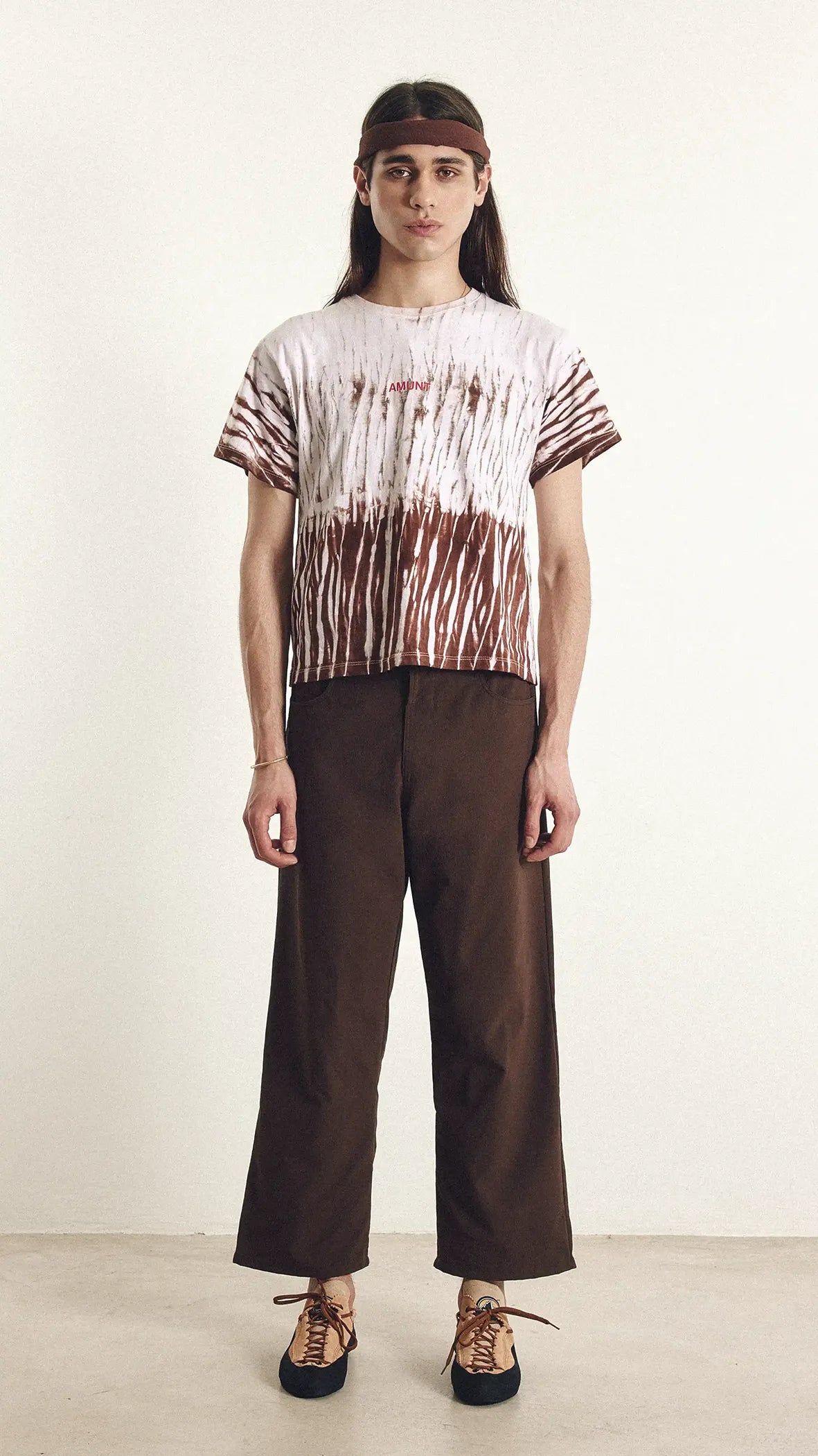 Person wearing a tie-dye shirt and brown pants on a plain background