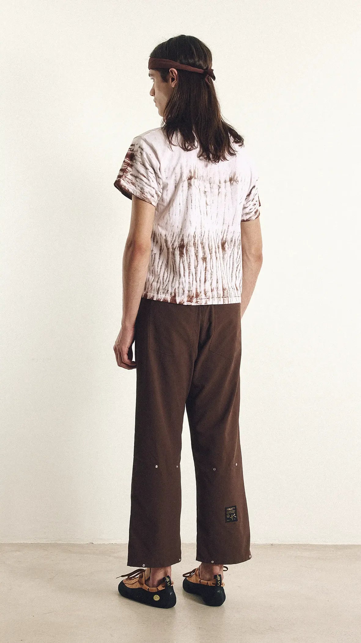 Person wearing a tie-dye shirt and brown pants against a white background