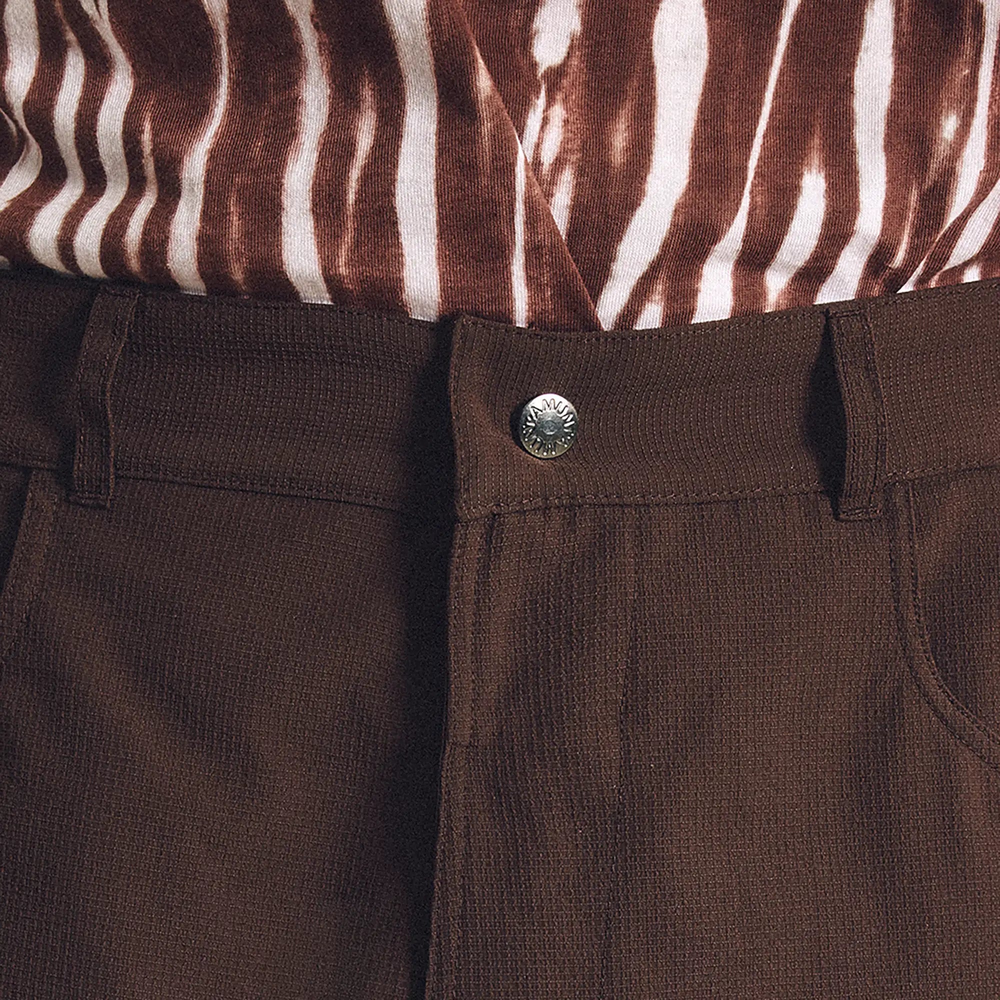 Close-up of brown pants with a button, zebra-patterned shirt in the background