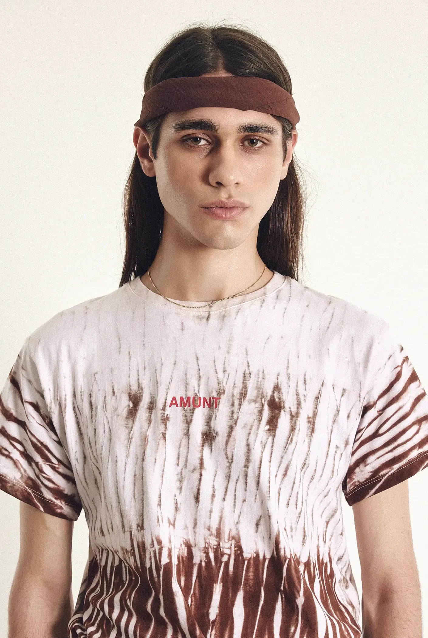 Person wearing a tie-dye shirt with 'AMEN' text and a headband on a plain background