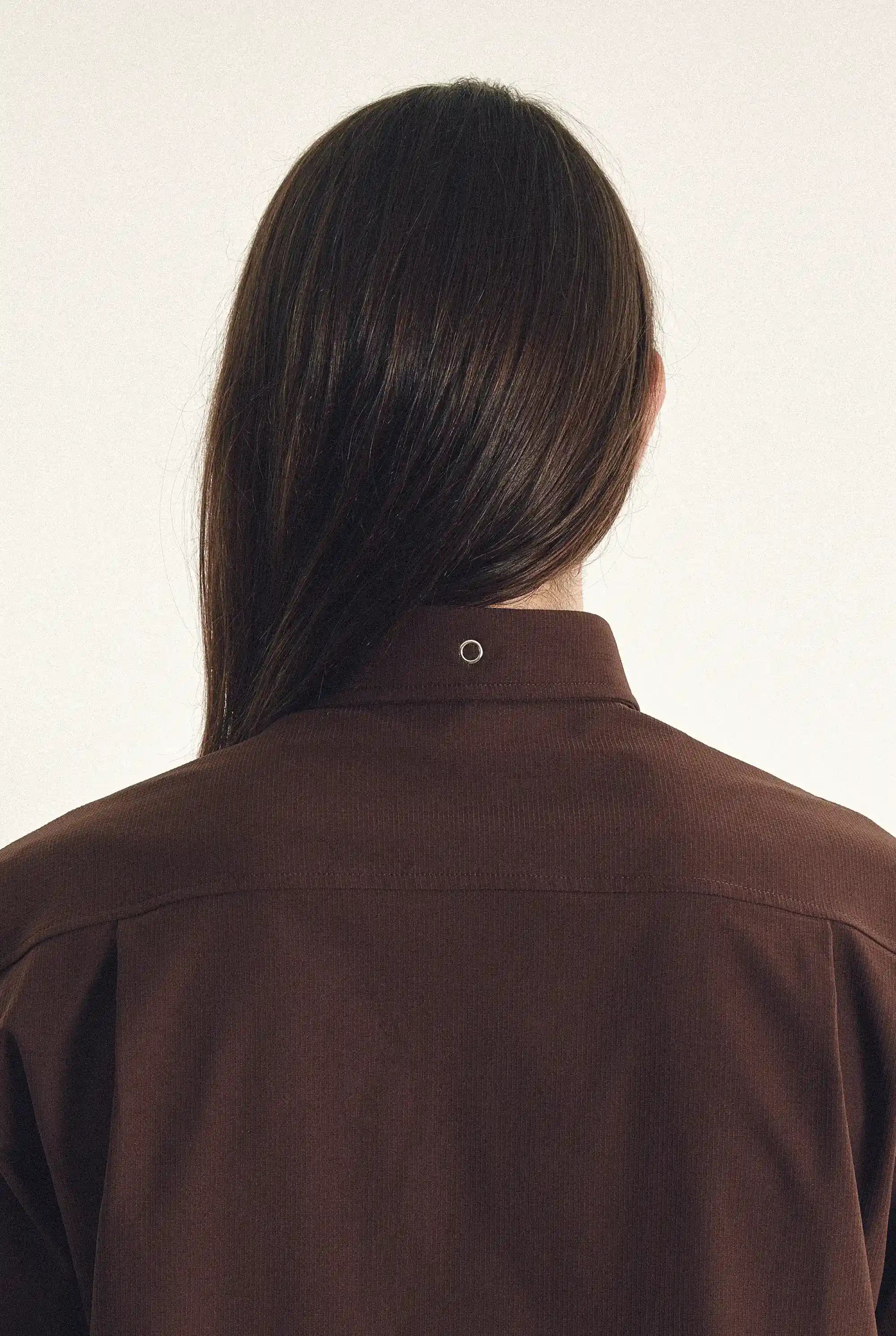 Back view of a person wearing a brown shirt against a white background