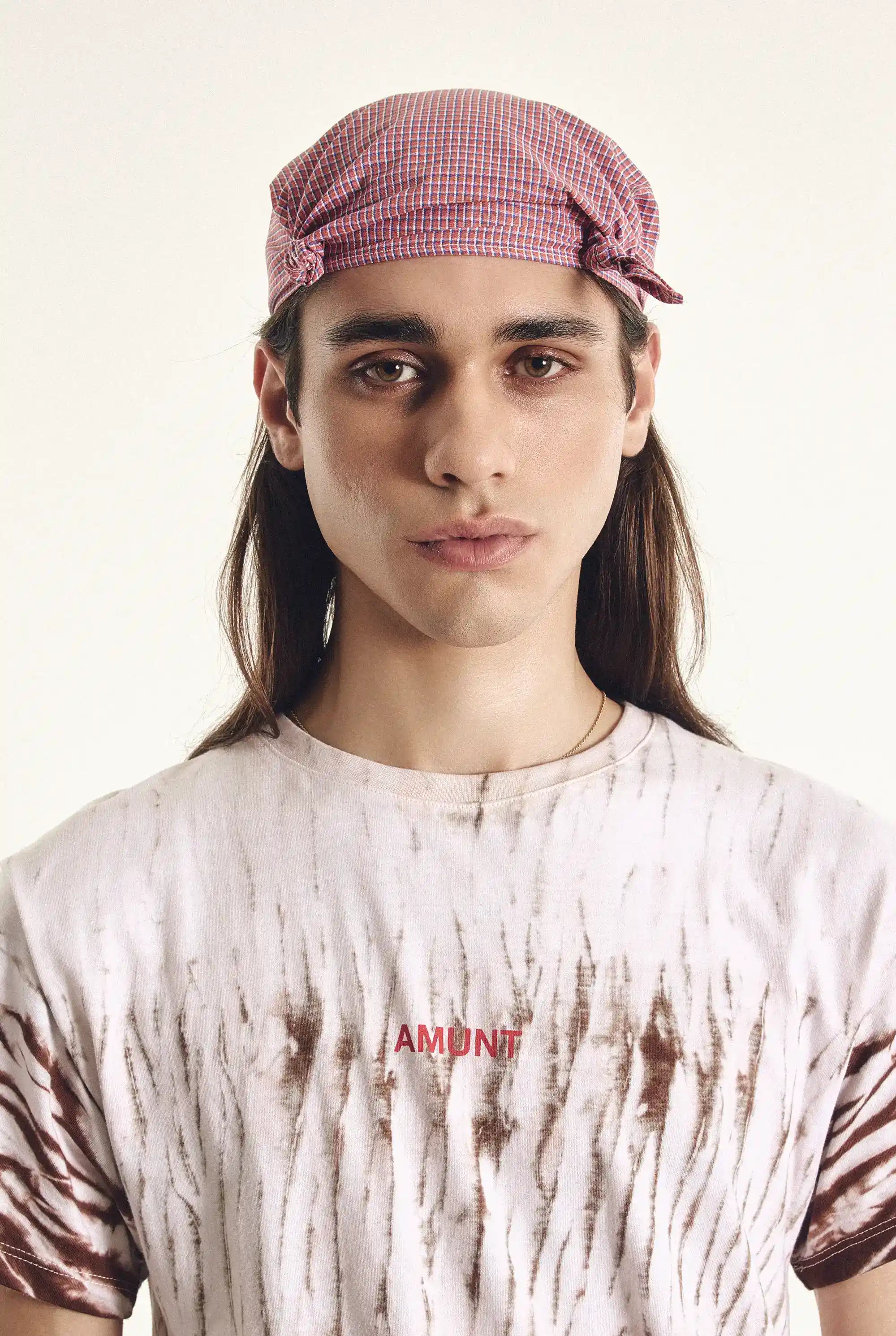 Person wearing a pink checkered hat and a tie-dye shirt with 'AMONT' branding.