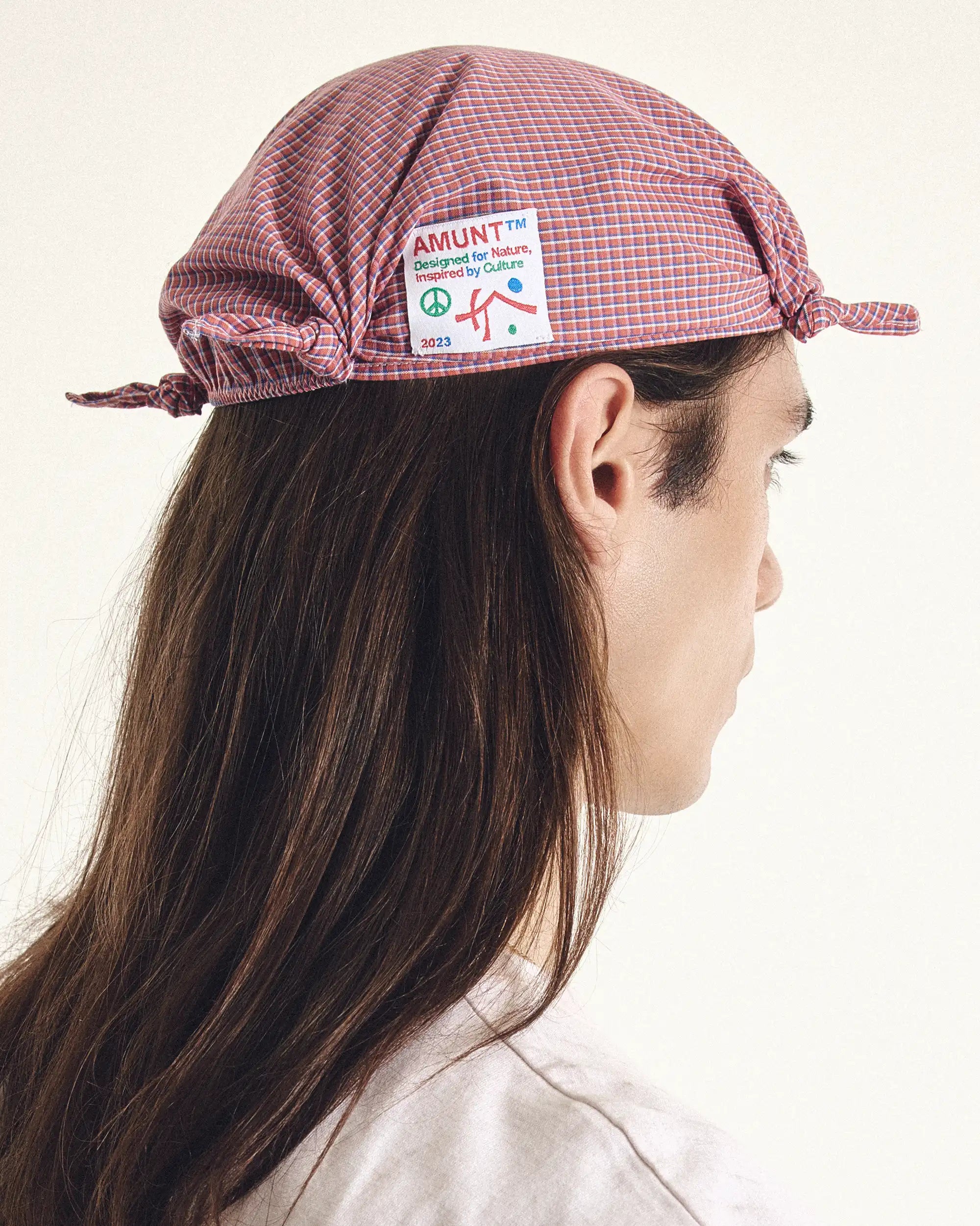 Person wearing a red checkered cap with a visible brand logo on a plain background