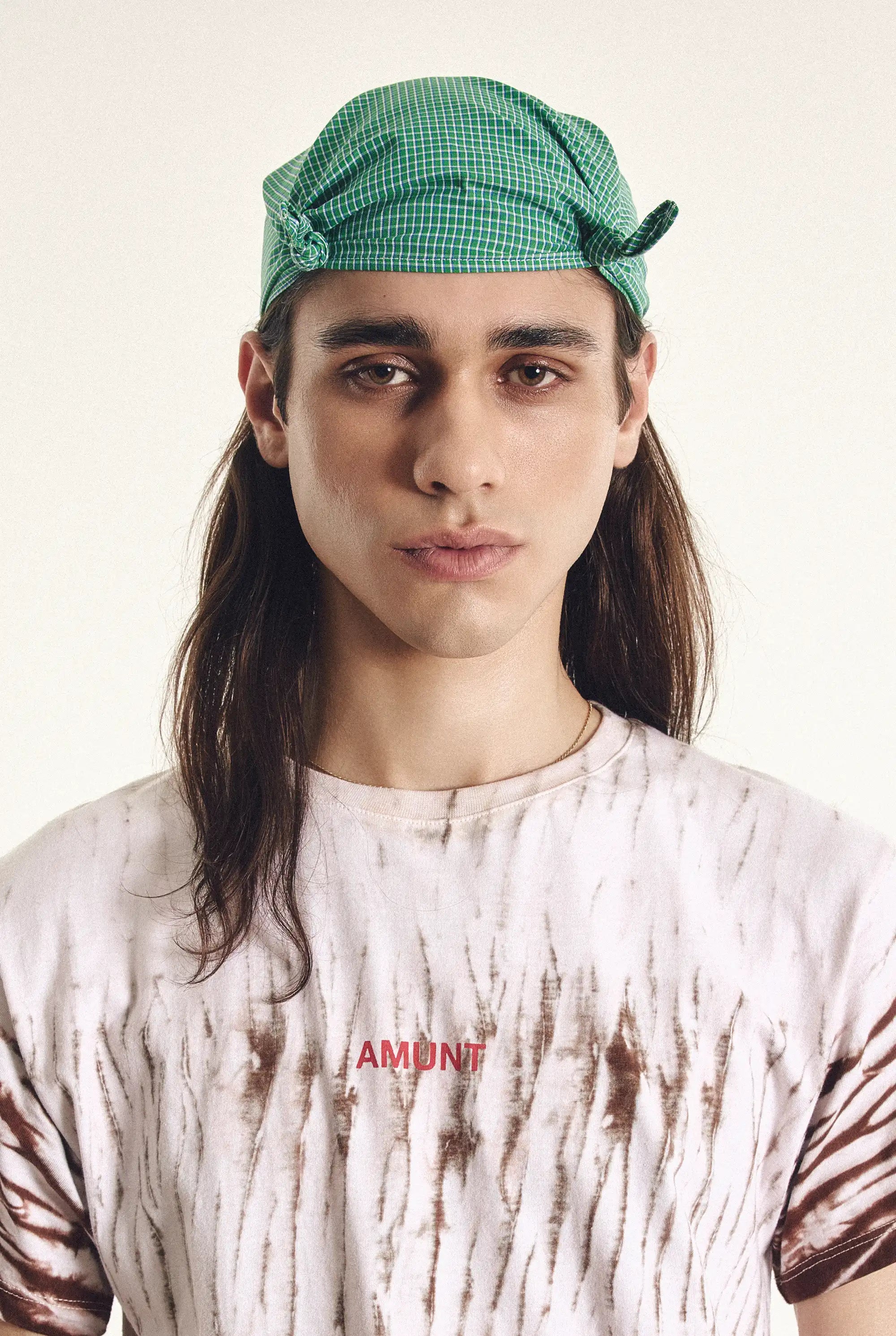 Person wearing a green checkered cap and a tie-dye shirt with 'AMUNT' text.