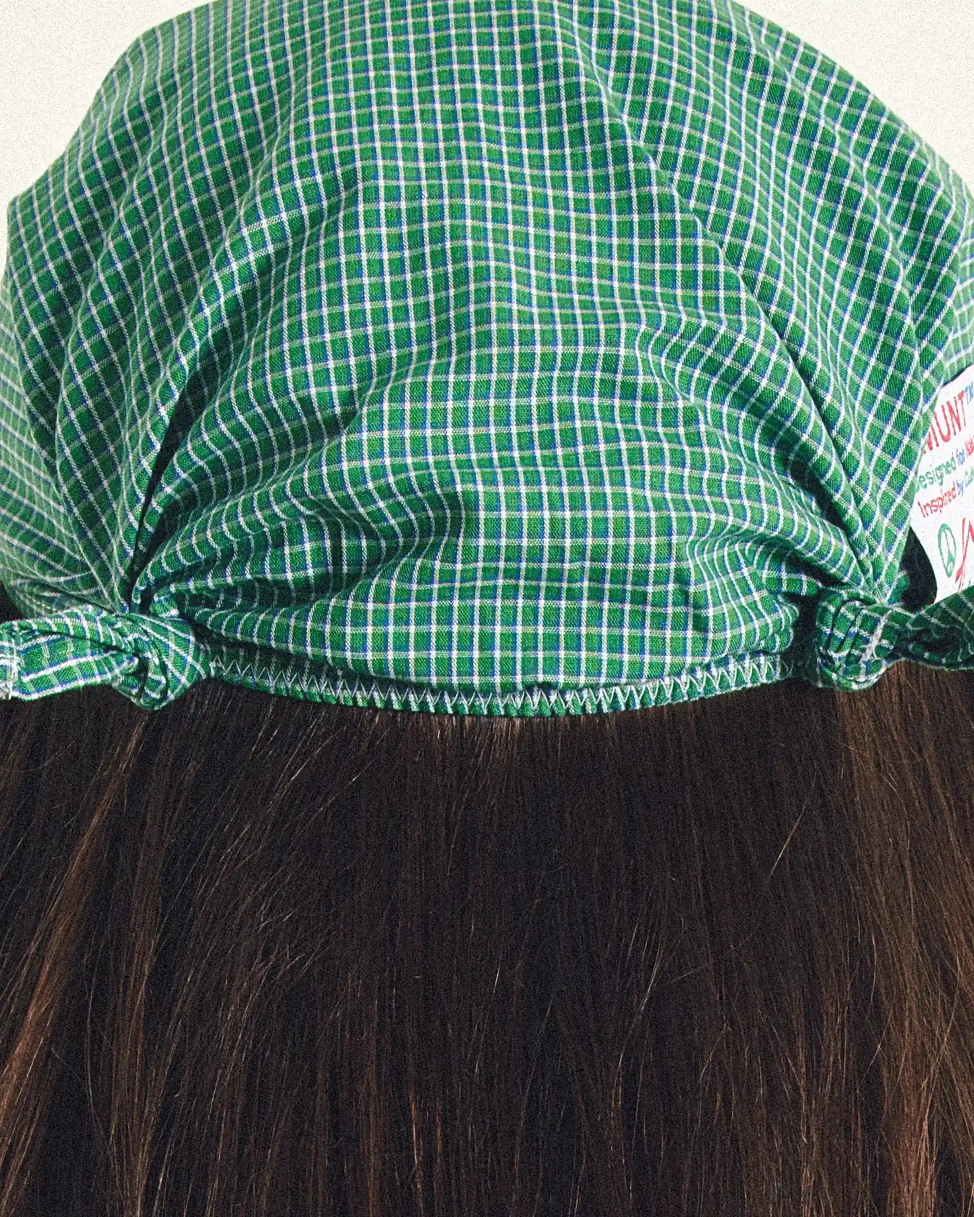 Green checkered cap on a wig with a visible brand label.