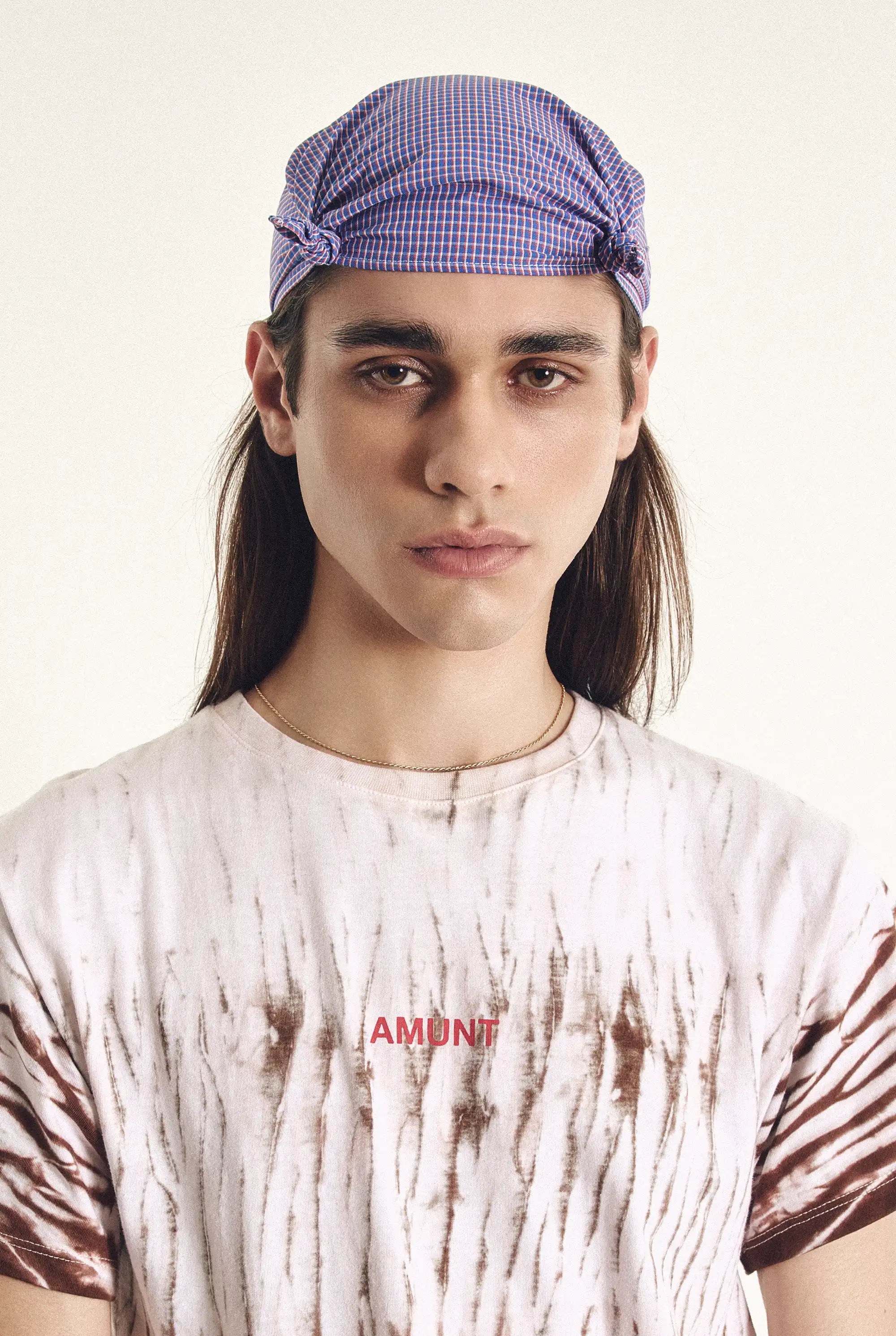 Person wearing a checkered cap and a tie-dye shirt with 'amunt' branding.