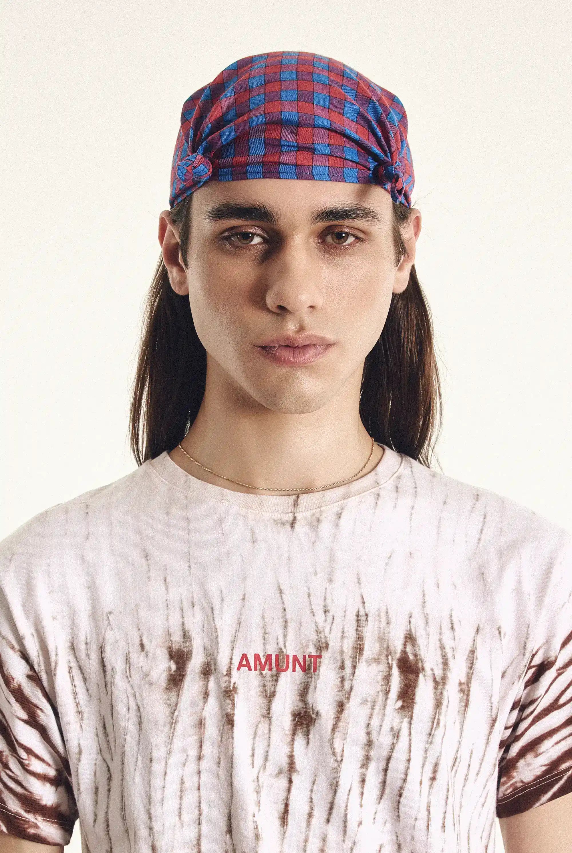 Person wearing a red and blue plaid cap with a white t-shirt featuring 'amunt' text.