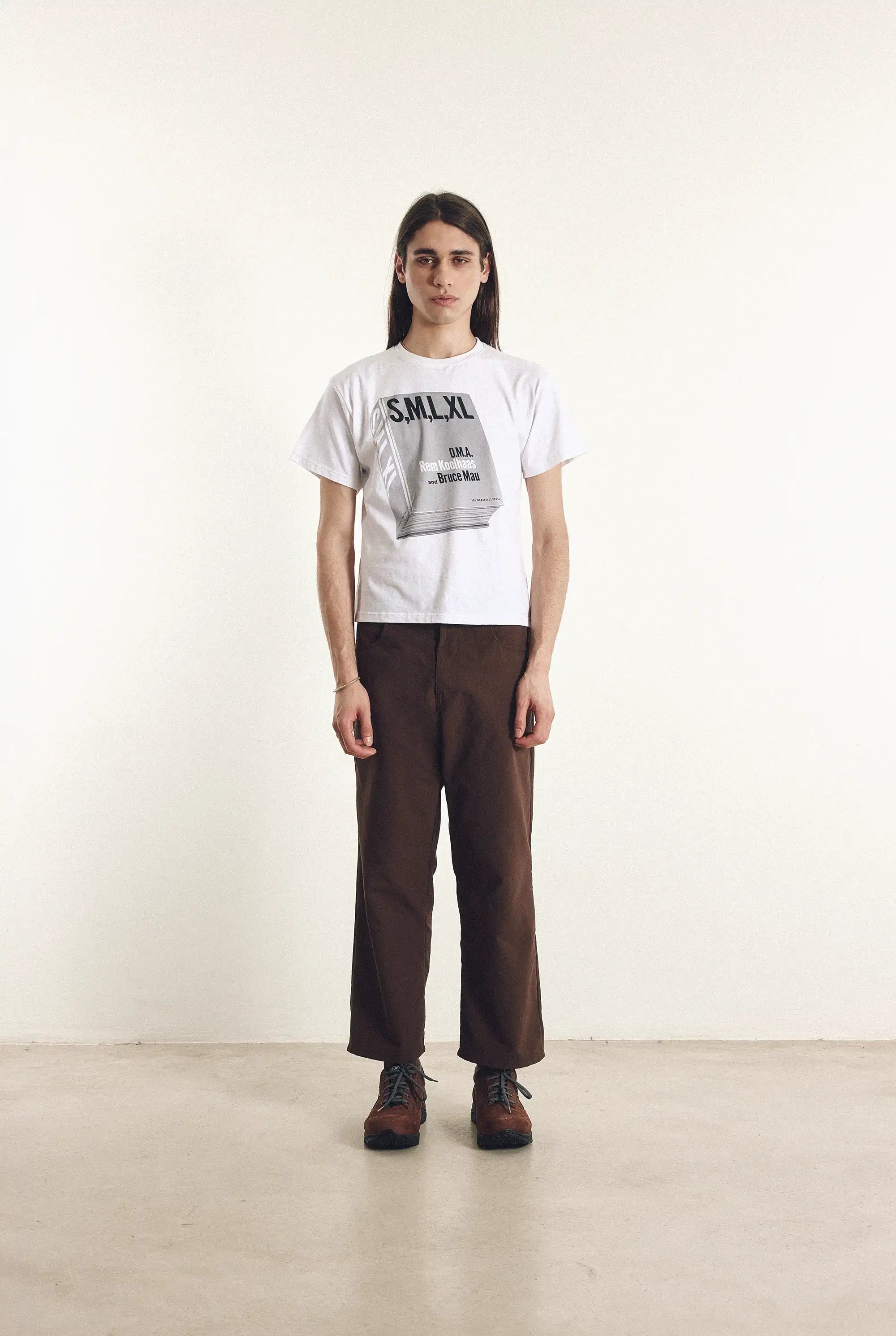 Person wearing a white t-shirt with text and brown pants on a plain background