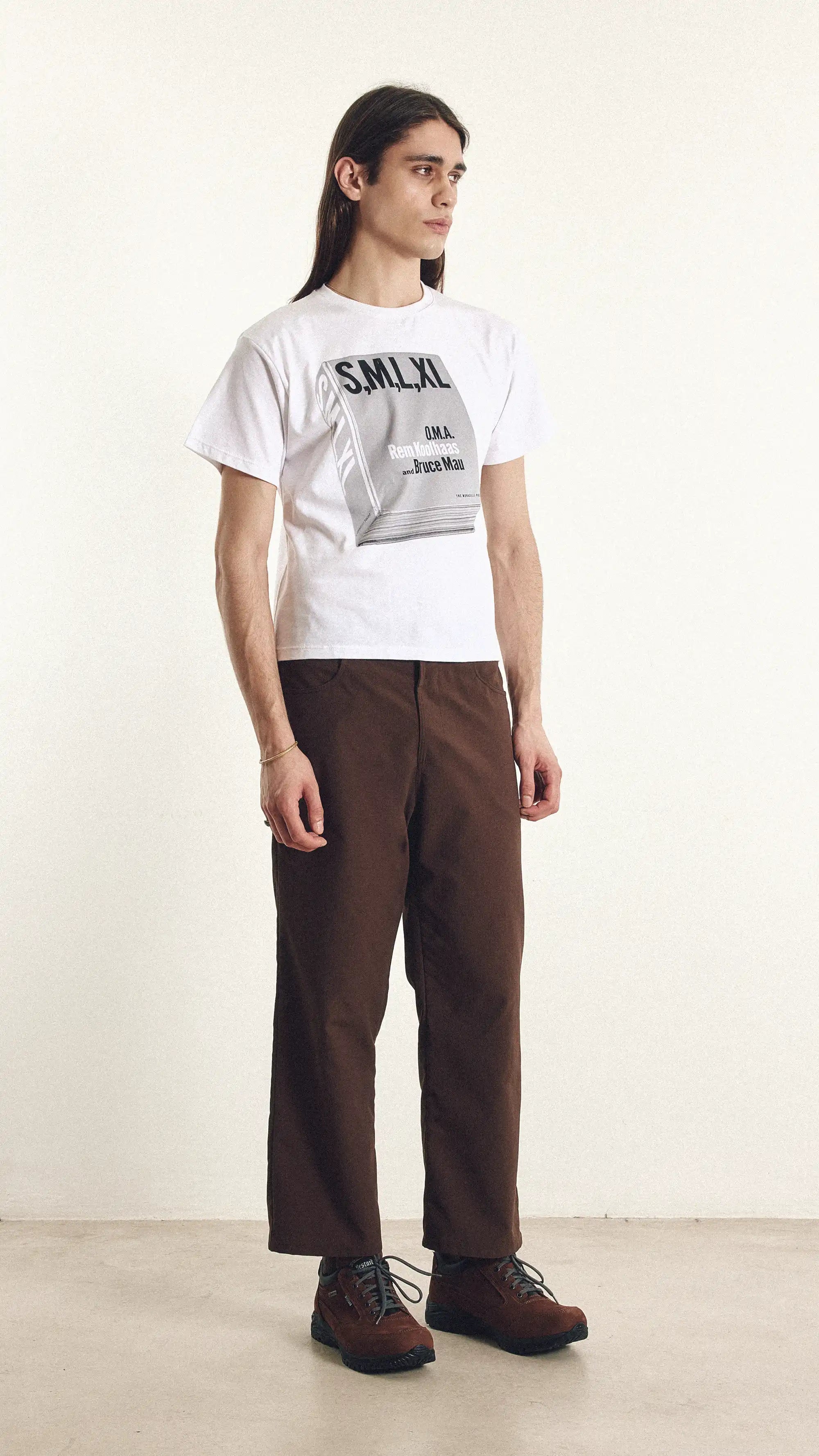 Person wearing a white t-shirt with text and brown pants on a plain background