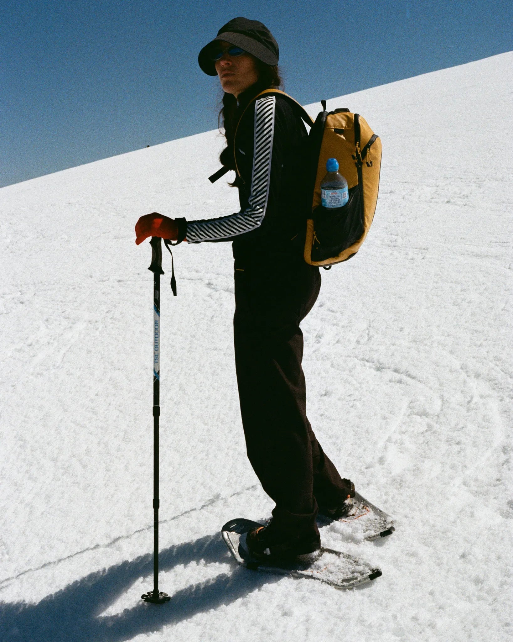 Person snowshoeing on a snowy landscape with a backpack and poles.