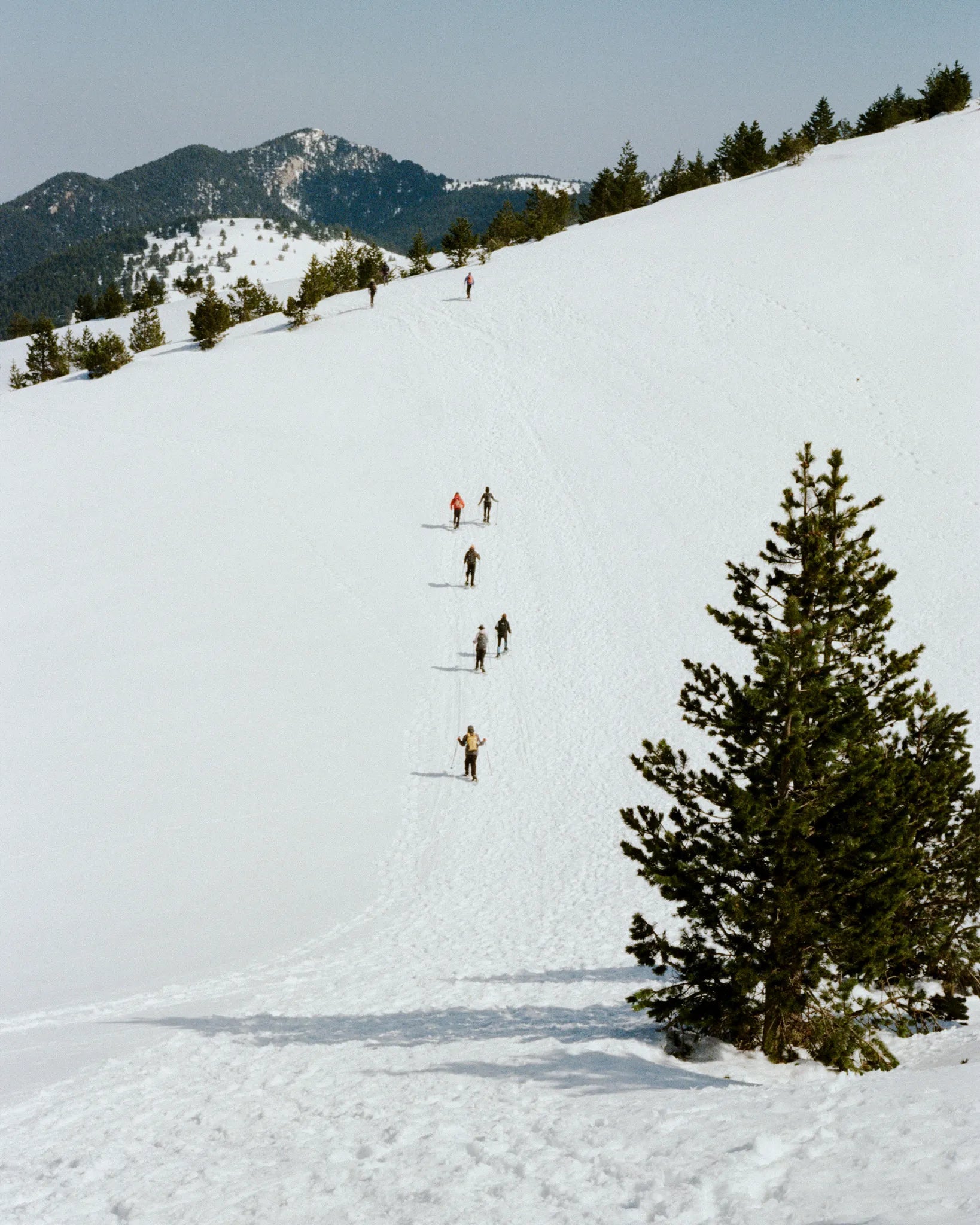 People skiing down a snowy slope with mountains in the background