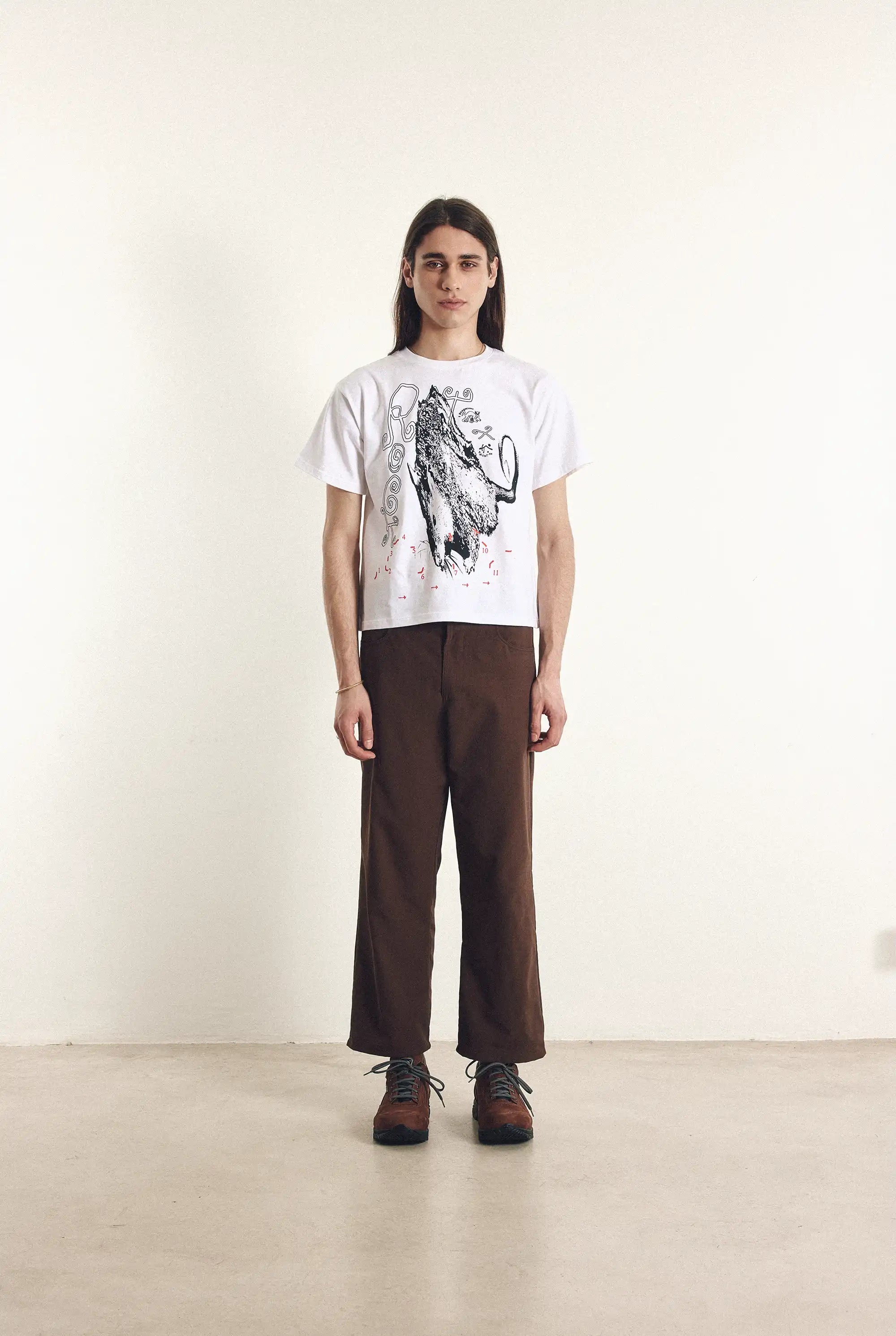 Person wearing a white t-shirt with an elephant graphic and brown pants on a plain background