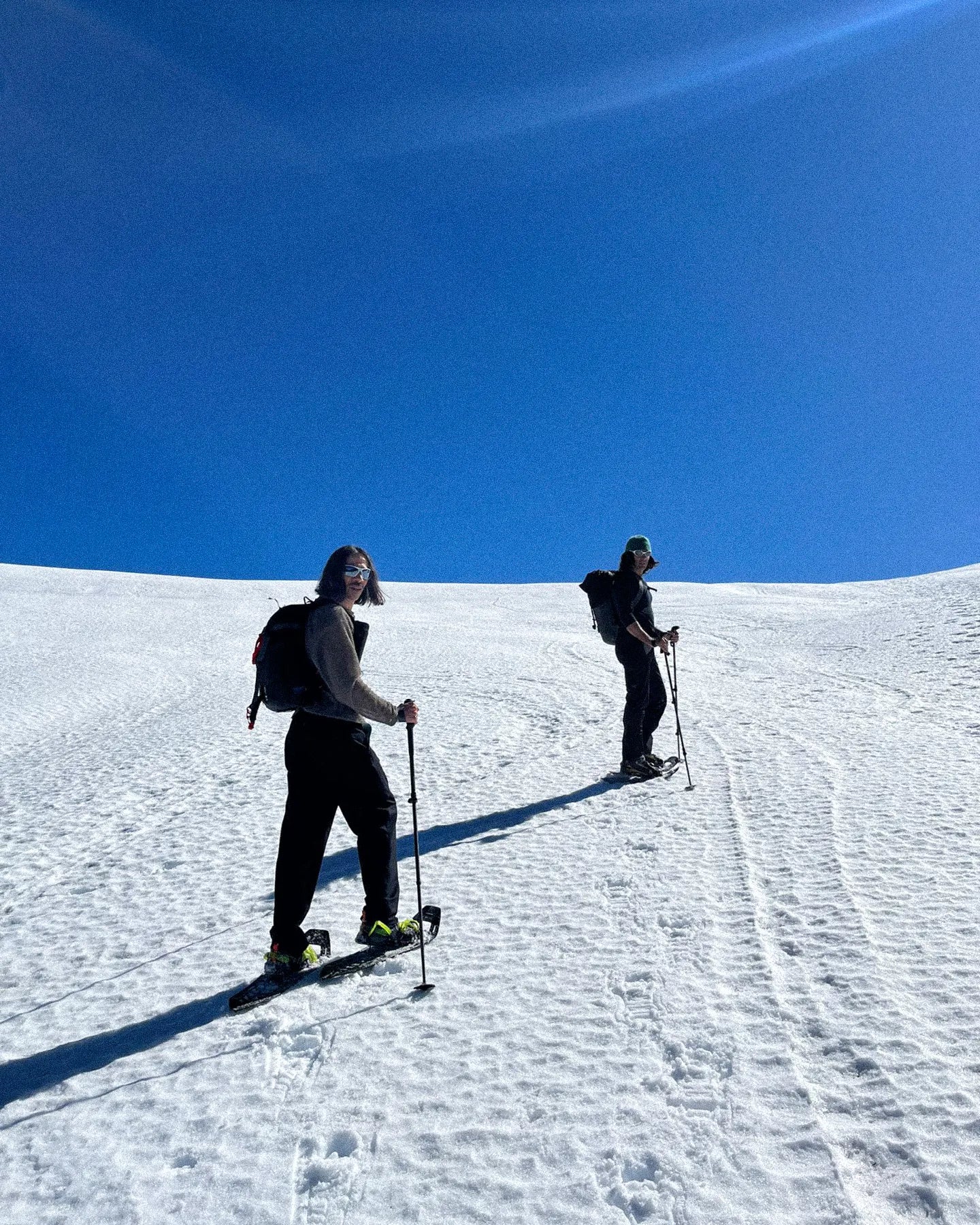 Two people skiing on a snowy slope with a clear blue sky above.