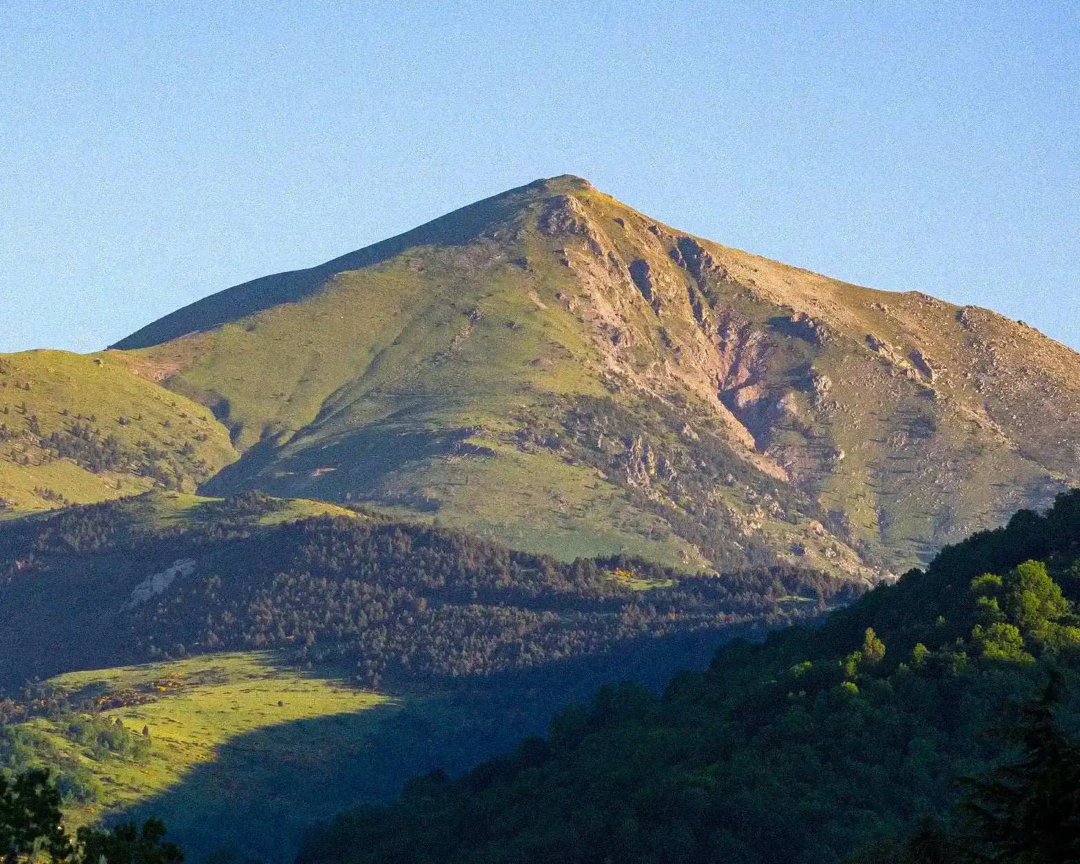 Mountain peak with greenery under a clear blue sky
