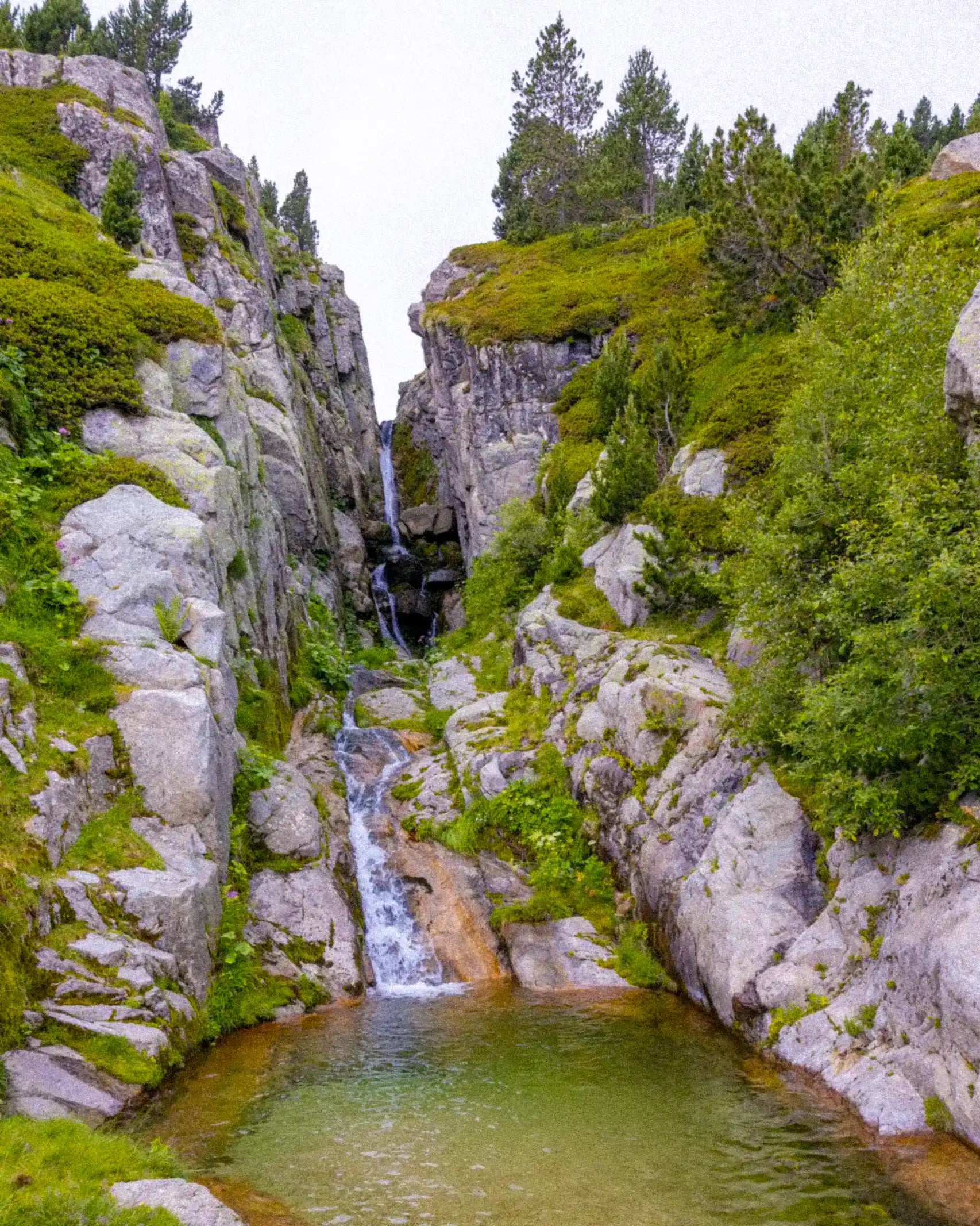 Waterfall cascading down rocky cliffs into a pool surrounded by greenery