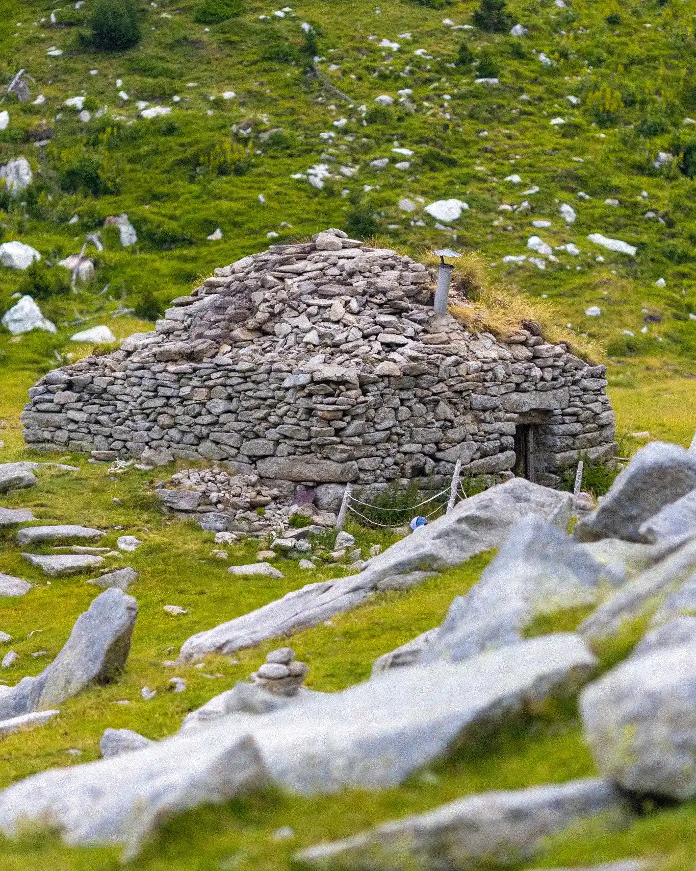Stone hut in a grassy field with scattered stones