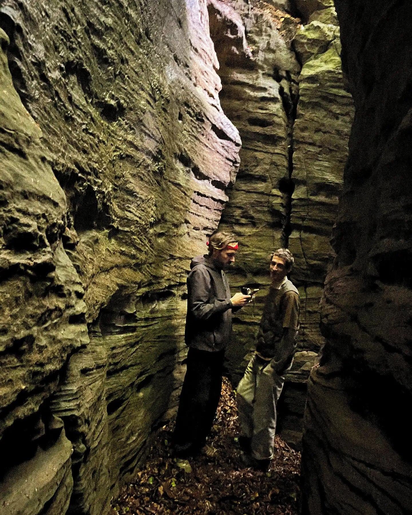 Two people exploring a narrow rocky passageway.