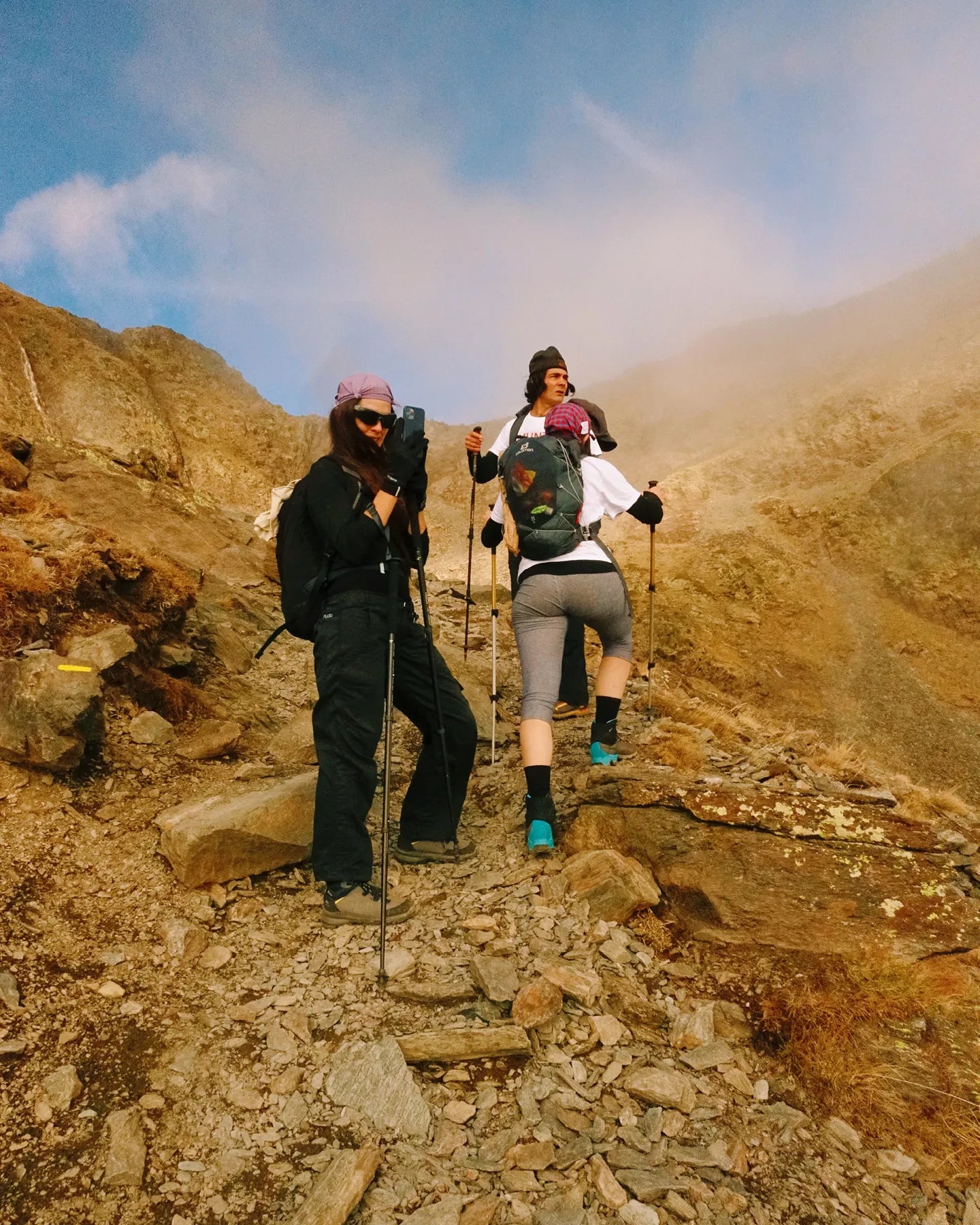 Two hikers on a rocky mountain trail with backpacks and hiking poles.