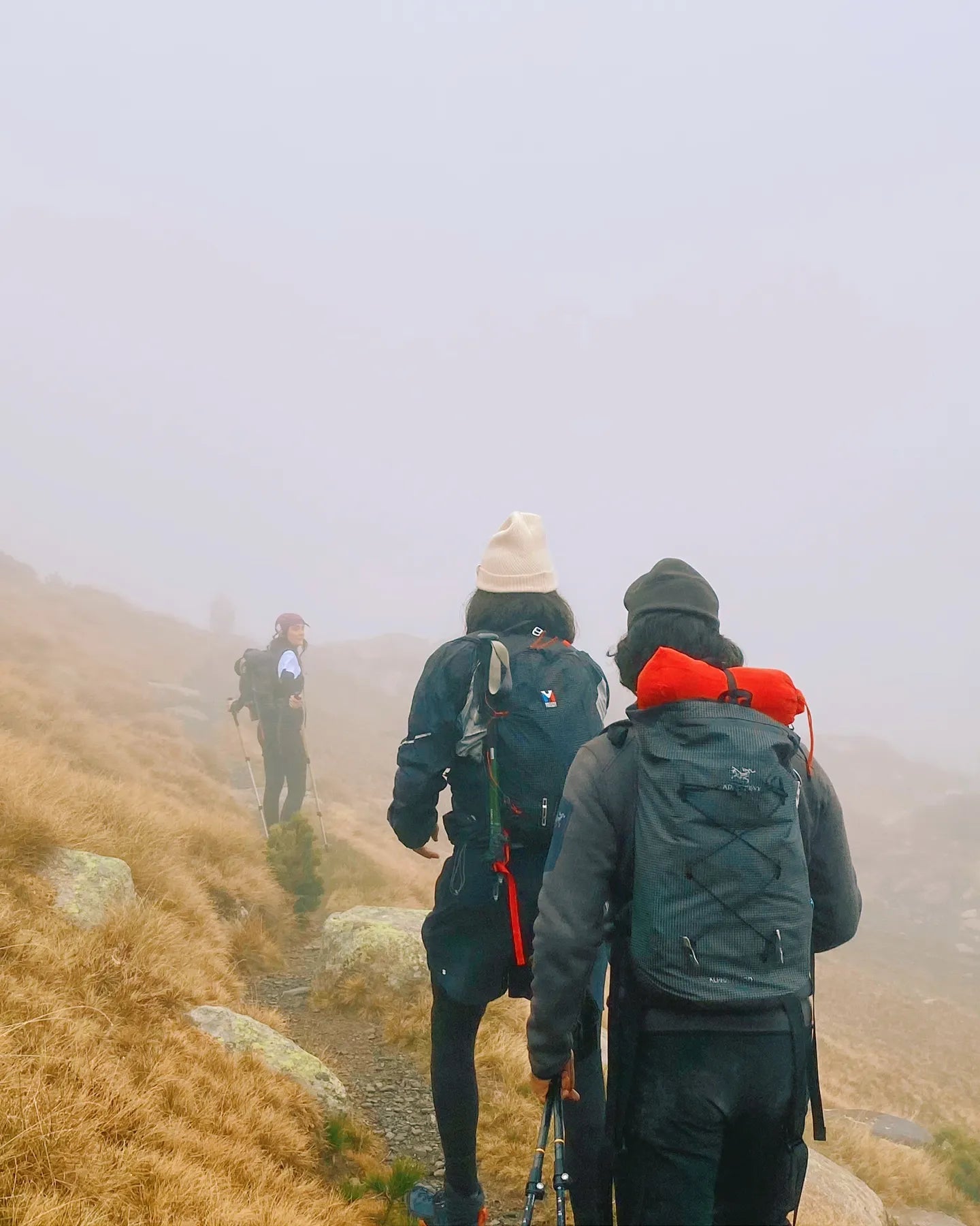 Two hikers on a foggy mountain trail with backpacks and hats.