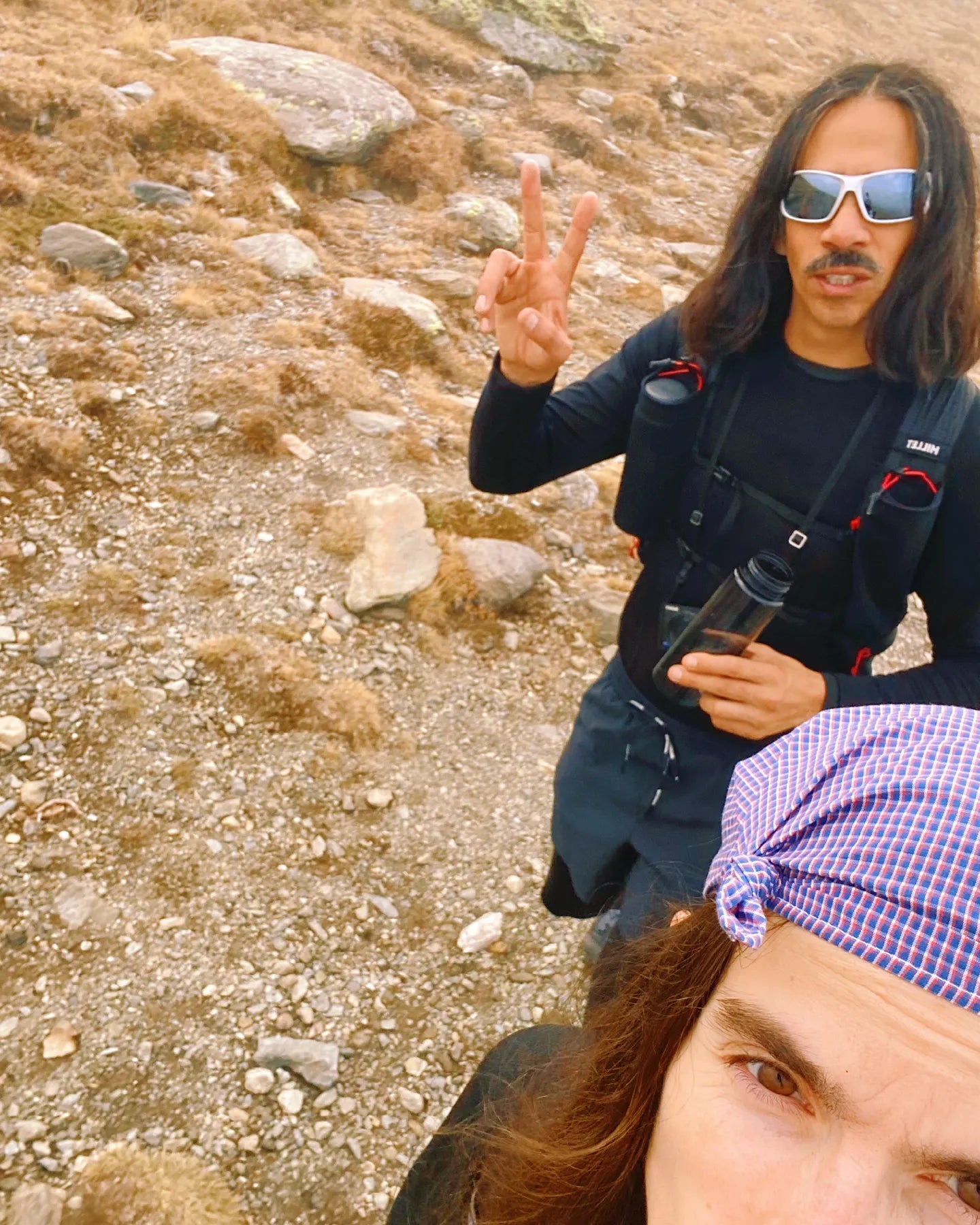 Person with a backpack and sunglasses standing on a rocky trail