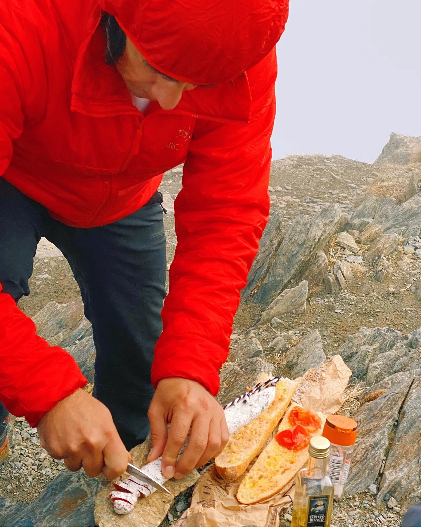 Person in a red jacket preparing food on a mountain top