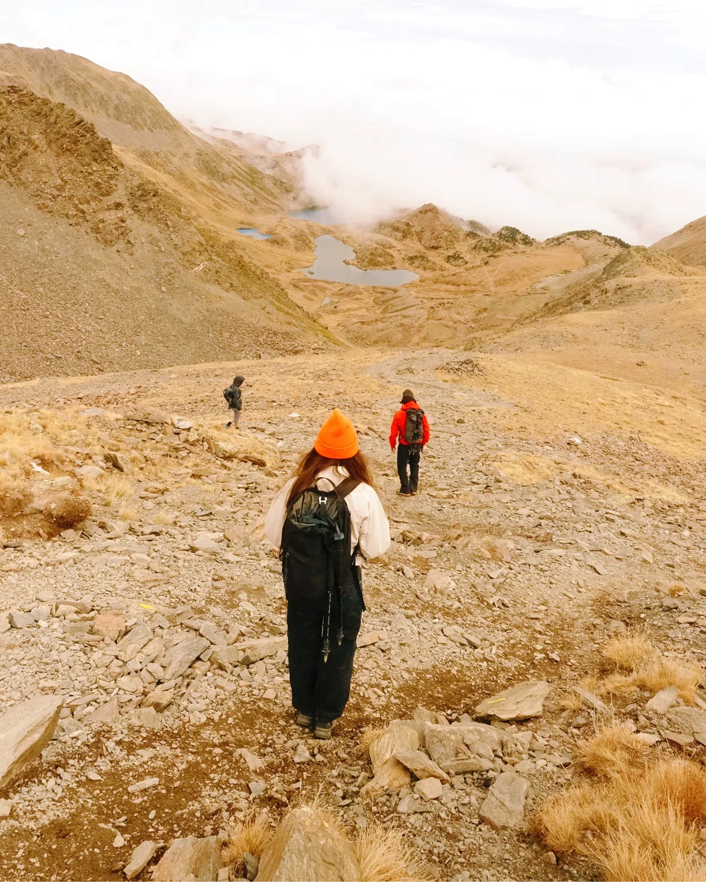 three hikers standing backwards in the middle of a rocky field